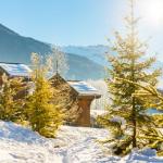 Slide Chalets en bois sous la neige aux Fermes de Samoëns by Ateya, avec vue sur les montagnes ensoleillées.