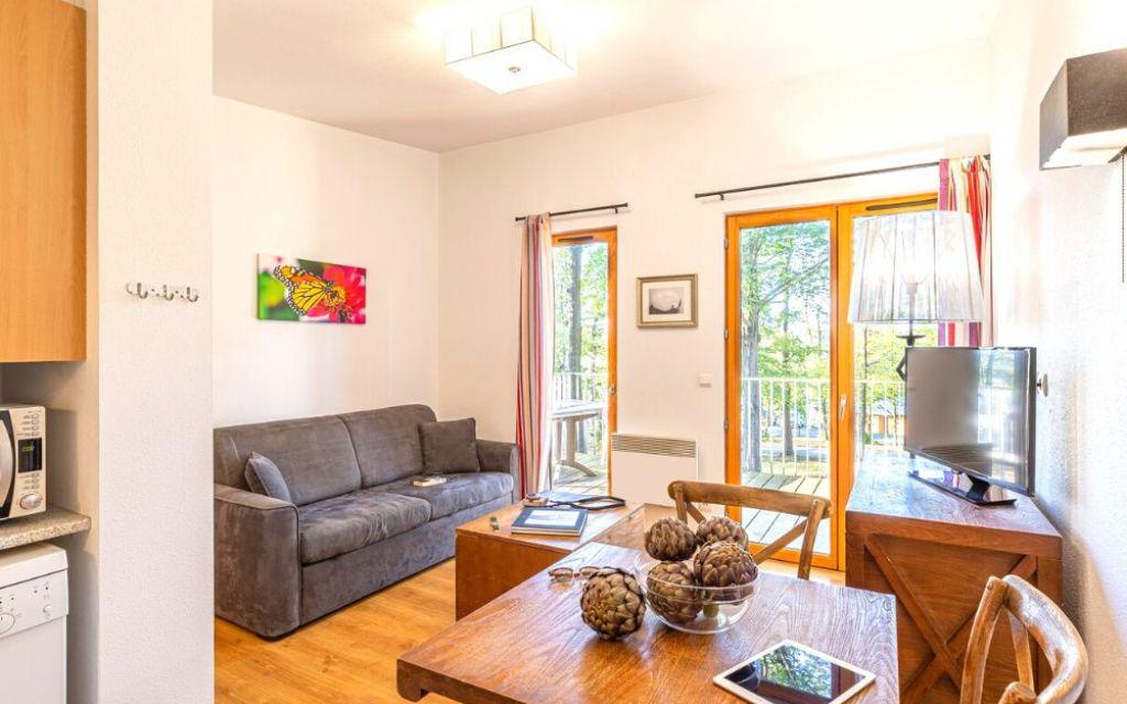 Slide Salon intérieur d’un cottage au Valjoly avec canapé, coin repas en bois, télévision et baie vitrée ouvrant sur la terrasse