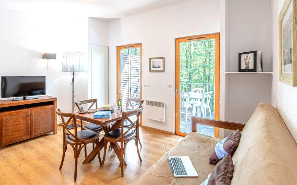 Slide Espace salon d’un cottage au Valjoly avec canapé, coin repas en bois, télévision et accès direct à la terrasse extérieure