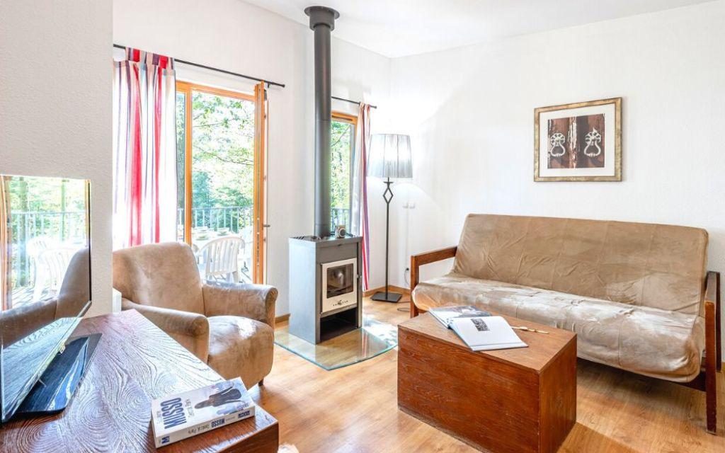 Slide Salon d’un cottage 3 pièces pour 6 personnes au Valjoly avec canapé, fauteuil, poêle à bois et terrasse donnant sur la nature