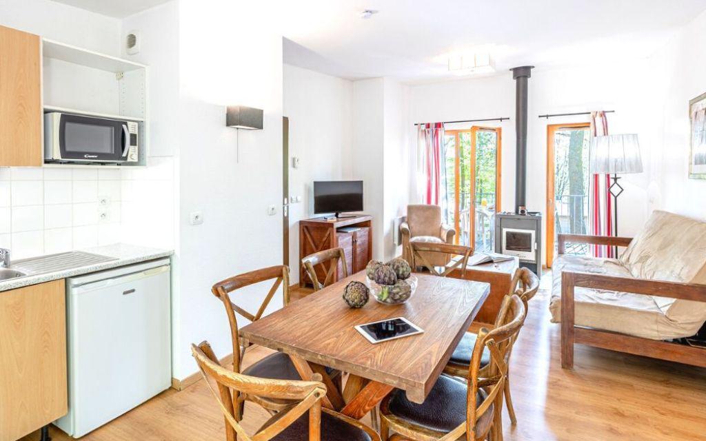 Slide Salon d’un cottage 3 pièces pour 6 personnes au Valjoly avec sallle à manger avec tables et chaises canapé, fauteuil, poêle à bois et terrasse donnant sur la nature