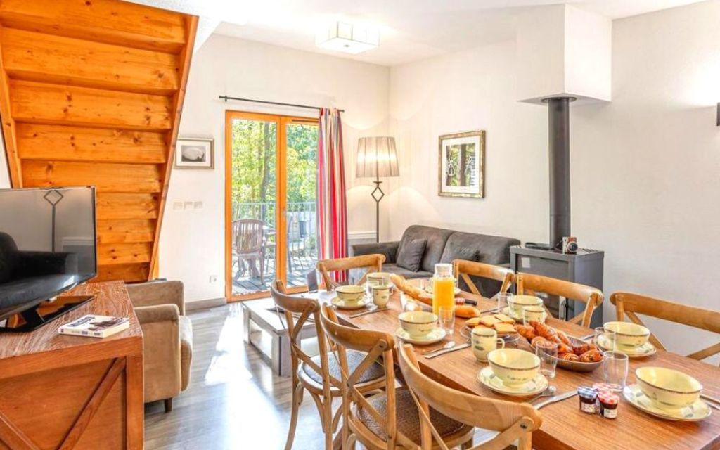 Slide Grand séjour d’un cottage 4 pièces 8 personnes au Valjoly avec table familiale dressée pour le petit-déjeuner, canapé, poêle et accès terrasse