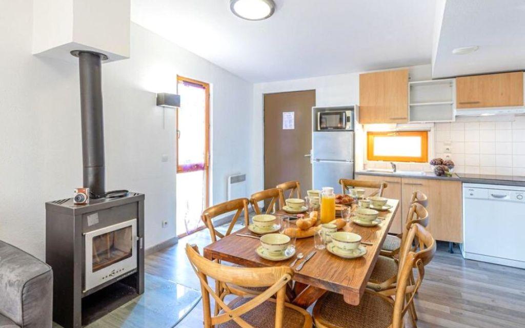 Slide Séjour d’un cottage 4 pièces 8 personnes au Valjoly avec cuisine équipée, poêle à bois et grande table familiale dressée pour le petit-déjeuner