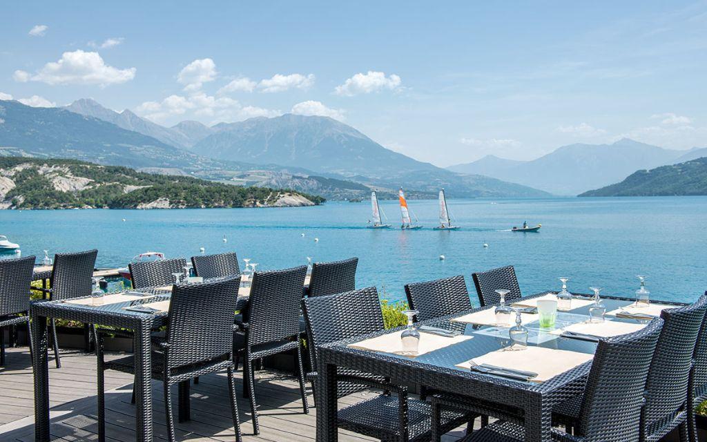 Slide Terrasse du restaurant de la résidence L’Écrin du Lac à Chorges avec vue sur le lac de Serre-Ponçon et ses voiliers