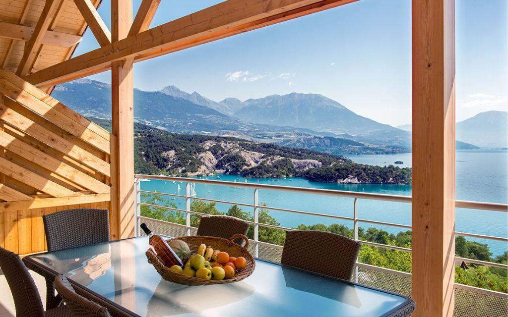 Slide alcon avec table et panier de fruits à la résidence L’Écrin du Lac à Chorges, offrant une vue imprenable sur le lac de Serre-Ponçon et les montagnes