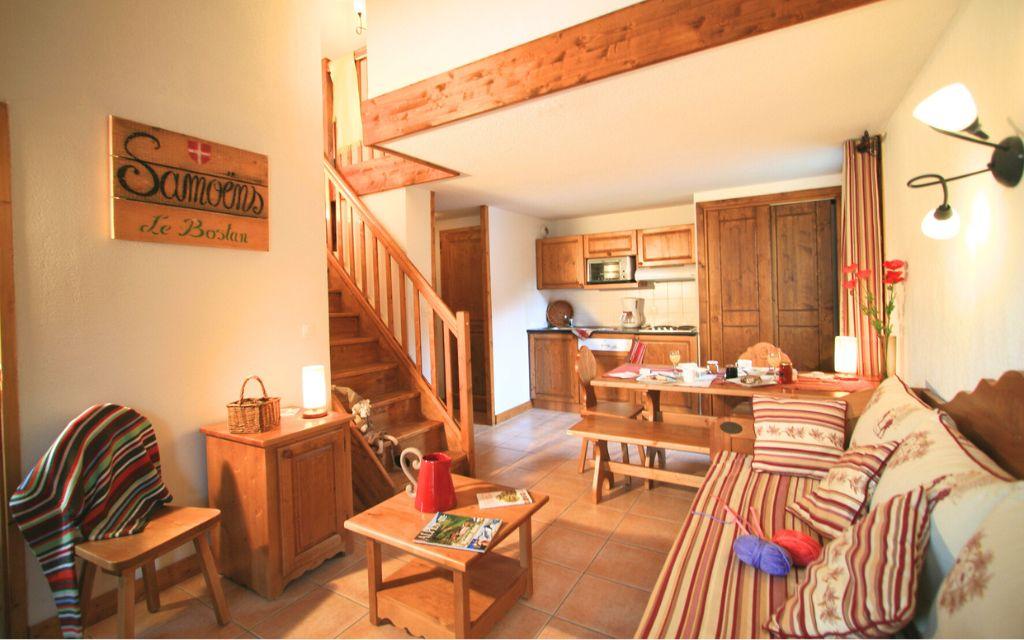 Slide Salon chaleureux avec escalier en bois et coin cuisine aux Fermes de Samoëns by Ateya Vacances