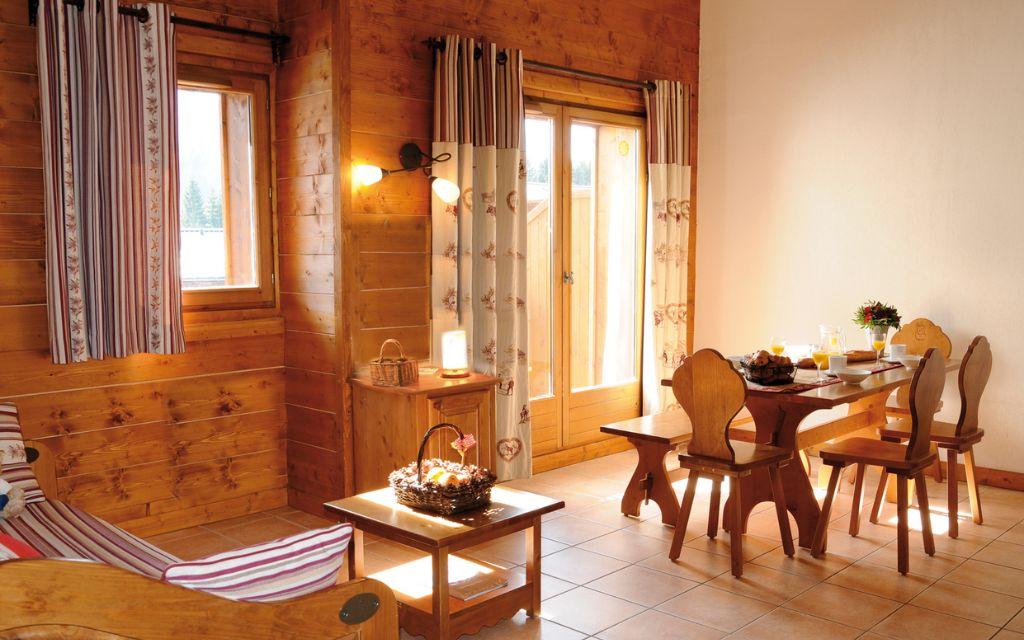 Slide Salon chaleureux avec coin repas et grandes fenêtres donnant sur les montagnes aux Fermes de Samoëns.