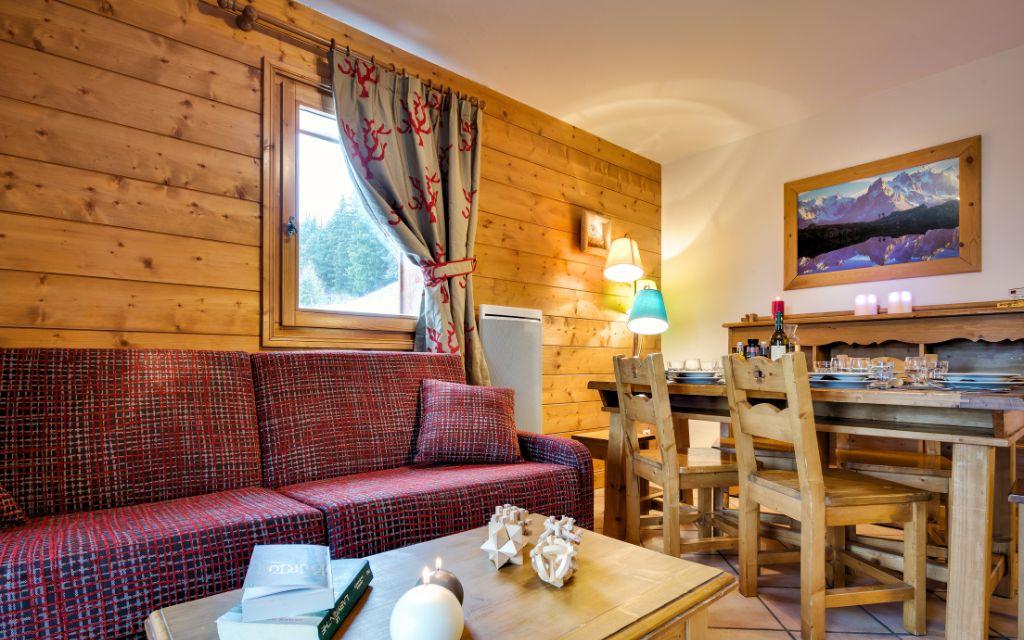 Slide Salon chaleureux en bois avec canapé rouge et coin repas au Hameau du Beaufortain aux Saisies