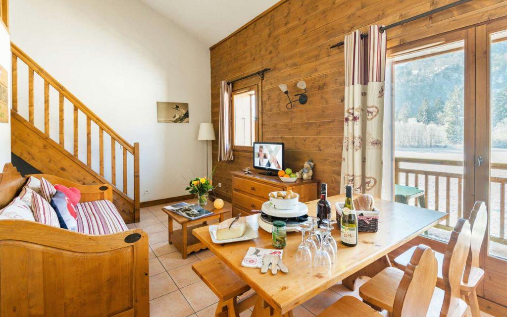 Slide living room with dining table and sofa and staircase leading to the upper floor in the Les Fermes de Samoens residence