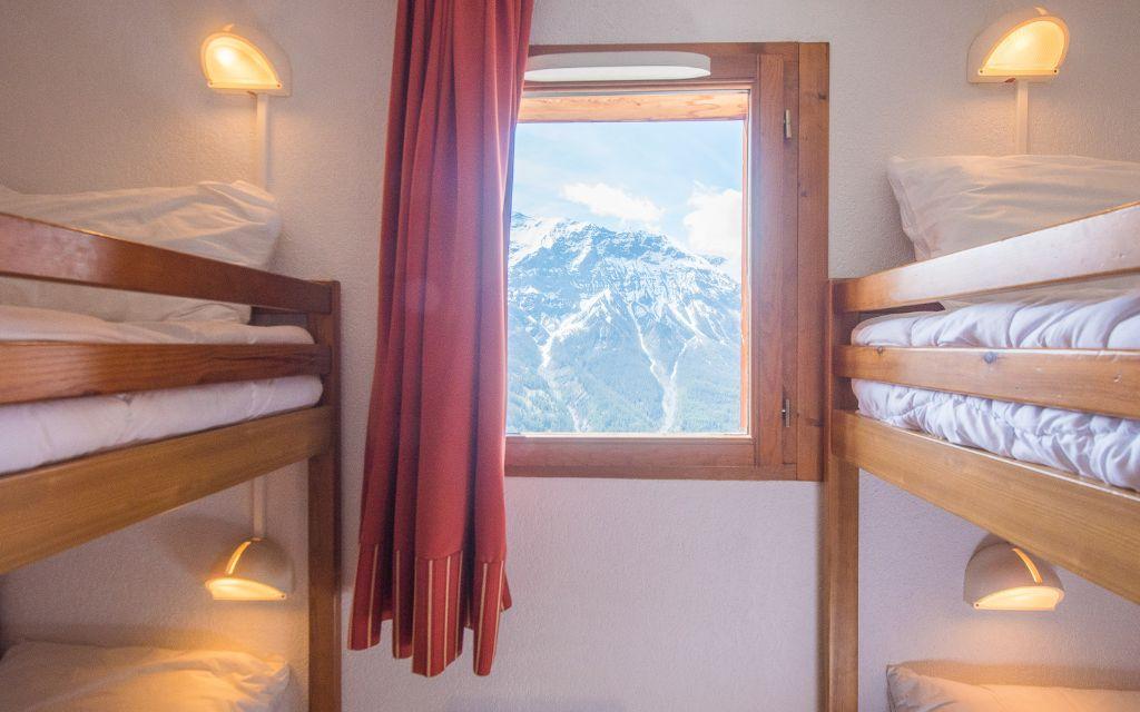 Slide Espace couchage avec list superposés et une fenêtre vue montagne sous la neige dans la résidence Les Etoiles d’Orion