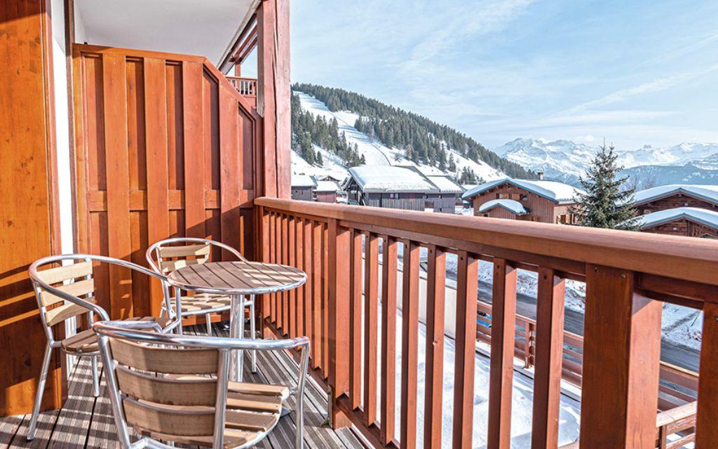 Slide Balcon avec petite table et chaises vue sur les montagnes enneigées à la résidence Les Chalets d’Emeraude