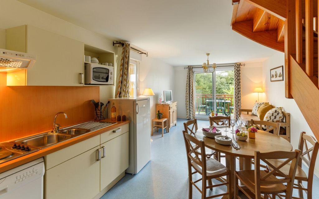 Slide Equipped open kitchen with dining table and lounge area in an apartment at Résidence Les Roches Douvres