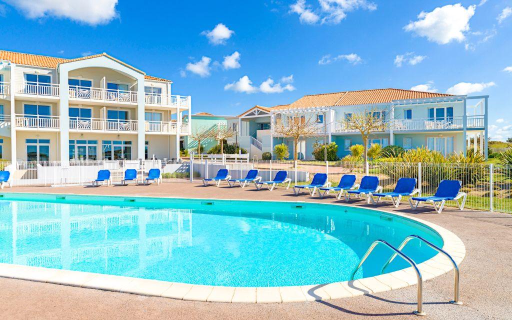 Slide Outdoor pool area surrounded by sun loungers and lush green gardens at the L’Estran residence in Les Sables-d’Olonne