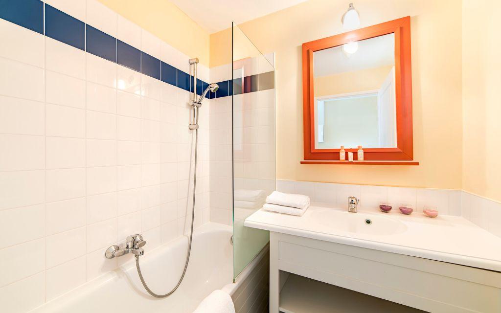 Slide Bathroom fitted with a bathtub, single washbasin, and mirror in one of the accommodations at the L’Estran residence in Les Sables-d’Olonne