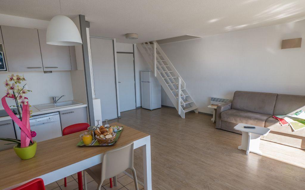 Slide Vue d’ensemble d’un séjour d’un appartement en duplex de la résidence Sokoburu avec coin repas, salon et cuisine ouverte