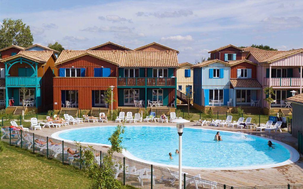 Slide Piscine centrale chauffée entourée d'ilots de maison au style cabane de pêcheur à la résidence Les Rives Marines au Teich