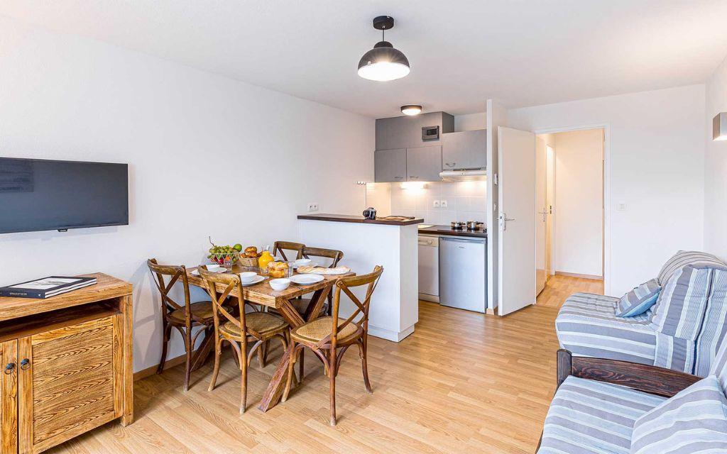 Slide Open-plan kitchen with a worktop overlooking the living area with sofa and television in the apartments of the Les Rives Marines residence in Le Teich