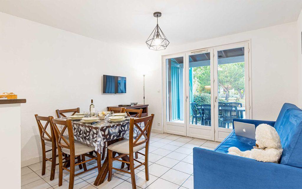 Slide Living area of a different layout, furnished with table, chairs and television, opening onto a terrace in one of the apartments at the Les Rives Marines residence in Le Teich