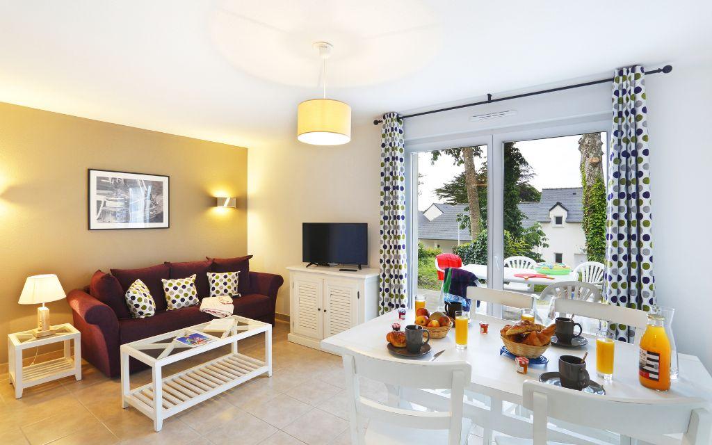 Slide Séjour d’une maisonnette avec coin salon et espace salle à manger au sein du Domaine de la Baie