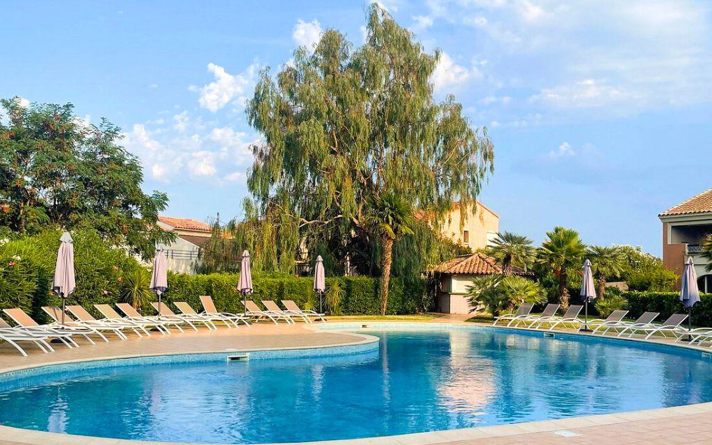 Slide Unheated outdoor swimming pool with sun loungers, surrounded by lush green gardens at the Sognu di Mare residence in Linguizzetta