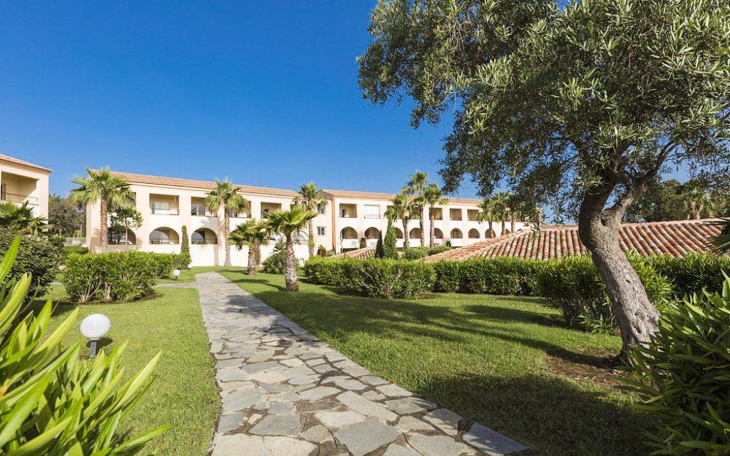 Slide Mediterranean-style residence with lush gardens featuring olive trees, shrubs, and palm trees, and a paved central walkway at the Sognu di Mare residence in Linguizzetta