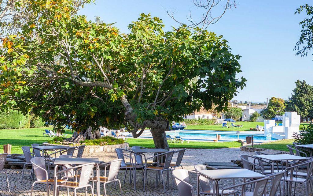 Slide Terrasse avec tables à manger et vue sur la piscine extérieure de la résidence Pedras del Rei