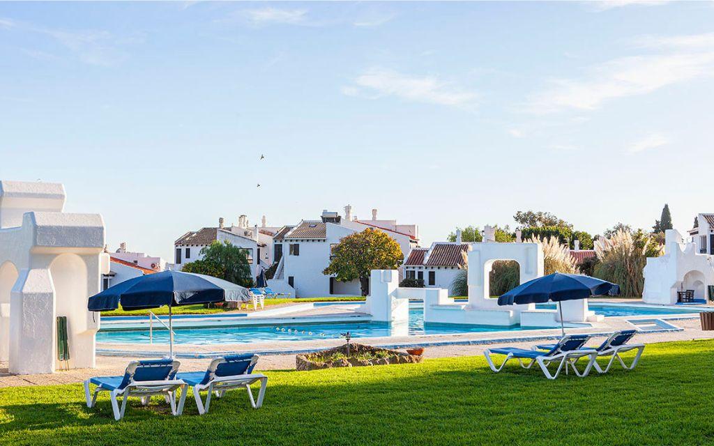 Slide General view of the unheated outdoor swimming pool at Pedras del Rei with sun loungers and the accommodation in the background