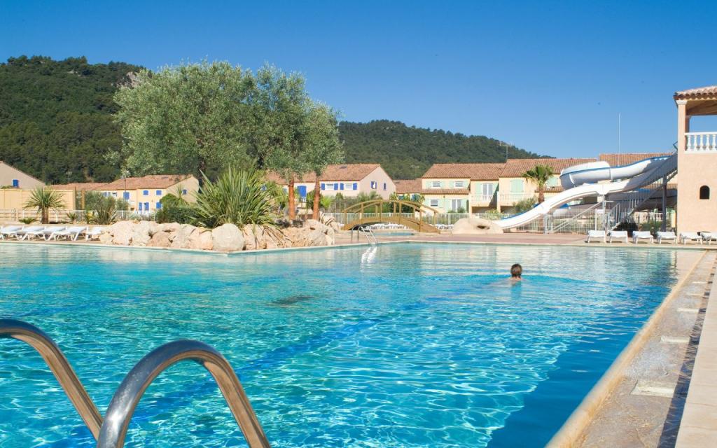 Slide Piscine extérieure de la résidence le clos des oliviers avec transats et pont au-dessus de l’eau