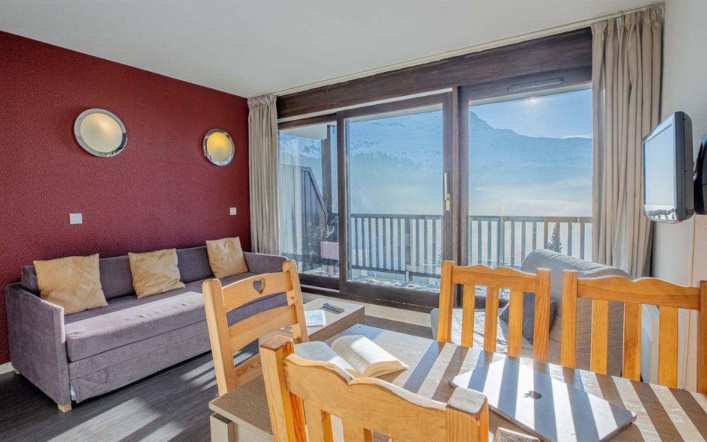 Slide Salon avec coin repas et TV ouvert sur un balcon avec vue sur les montagnes depuis les appartements Les Terrasses de Veret à Flaine