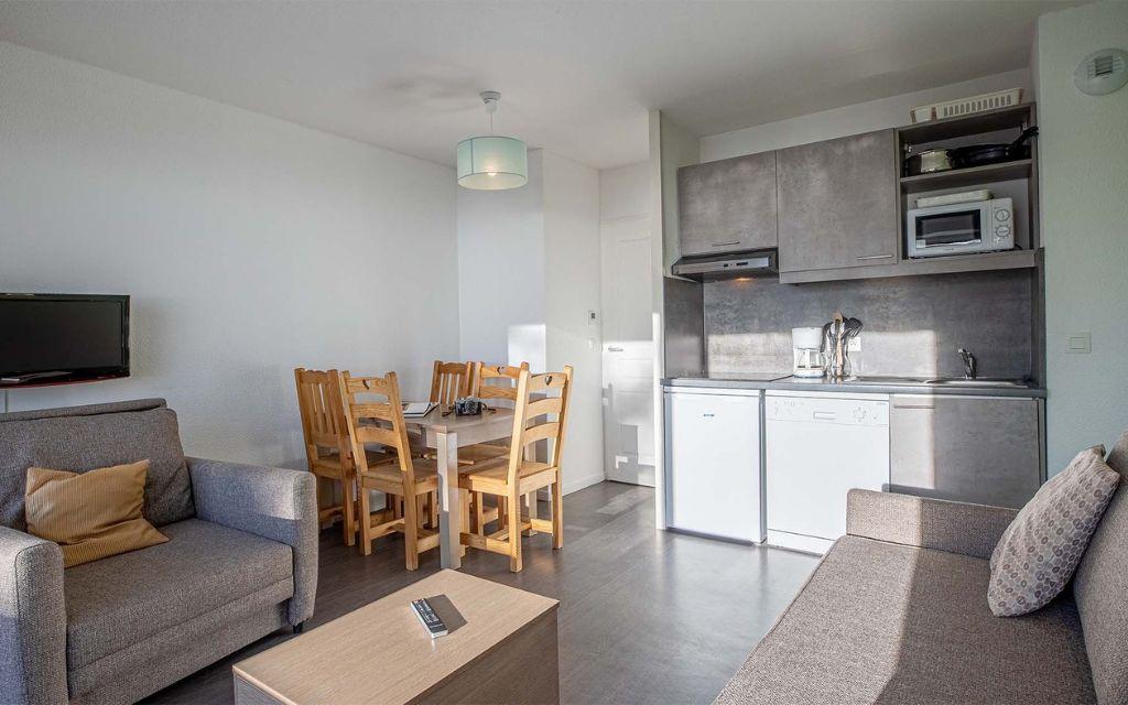 Slide Cuisine fonctionnelle avec salle de vie composée d'un canapé et TV dans les appartements des Terrasses de Veret à Flaine