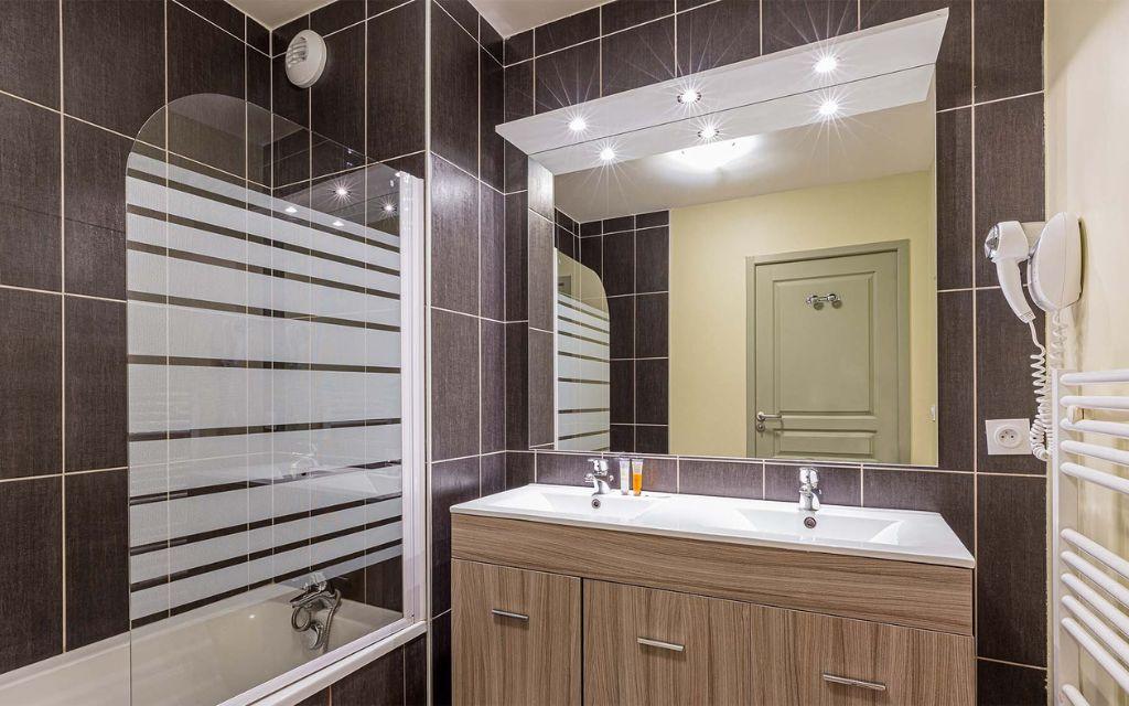 Slide Bathroom with a bathtub, mirror, and washbasin in the apartments at Les Épinettes Residence in Vaujany.