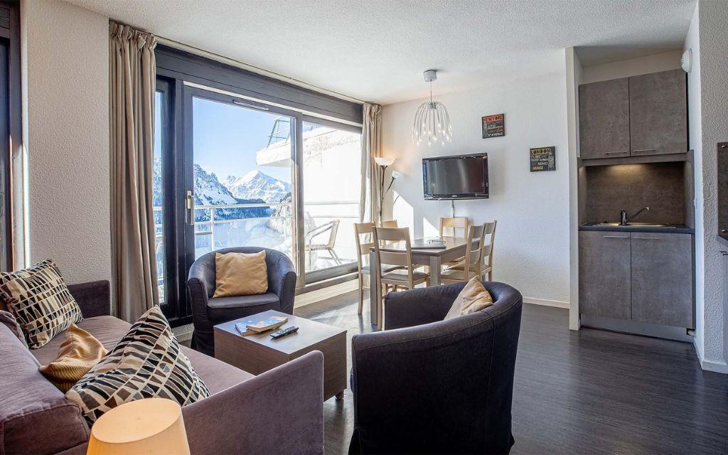Slide Salon avec coin repas et TV ouvert sur un balcon avec vue sur les montagnes depuis les appartements Les Terrasses de Veret à Flaine