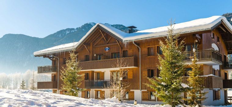 Résidence Les Fermes de Samoëns en hiver sous la neige avec sapins et montagnes en arrière-plan