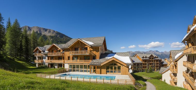 Résidence La Combe d’Or aux Orres 1800 en été avec piscine extérieure et vue sur les montagnes.