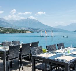 Terrasse du restaurant de la résidence L’Écrin du Lac à Chorges avec vue sur le lac de Serre-Ponçon et ses voiliers