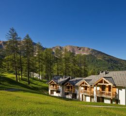 Résidence La Combe d’Or aux Orres 1800 en été, au cœur des montagnes et forêts verdoyantes.