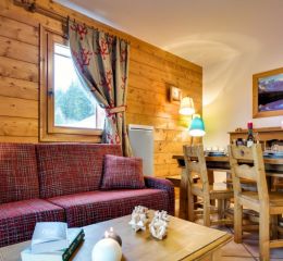 Salon chaleureux en bois avec canapé rouge et coin repas au Hameau du Beaufortain aux Saisies
