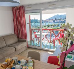 Salon avec canapé lit et balcon vue sur le port d’un logement de la résidence Sokoburu à Hendaye