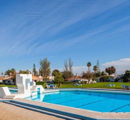 Unheated outdoor swimming pool of the Pedras del Rei residence with green space and sun loungers in the background