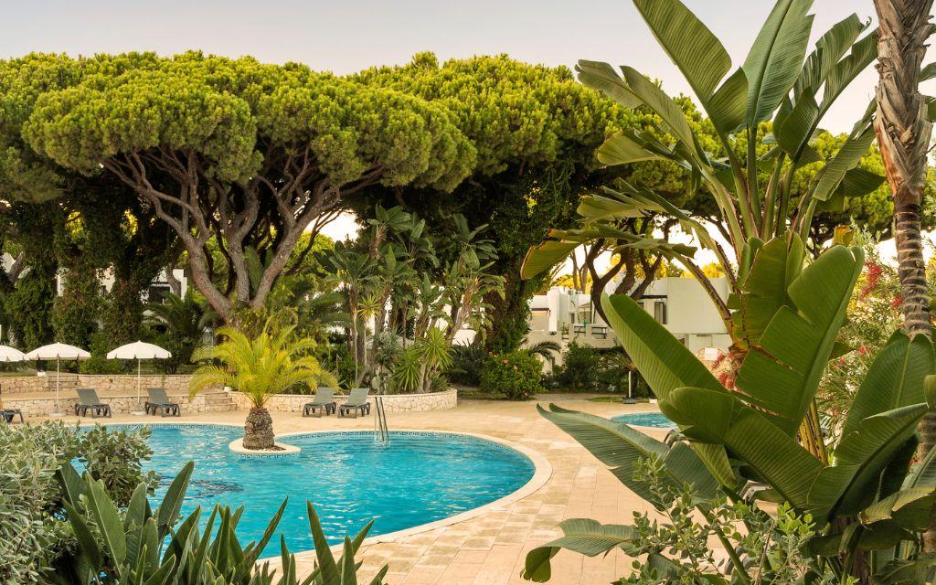 Slide Outdoor swimming pool with sun loungers and parasols in a tree-lined setting